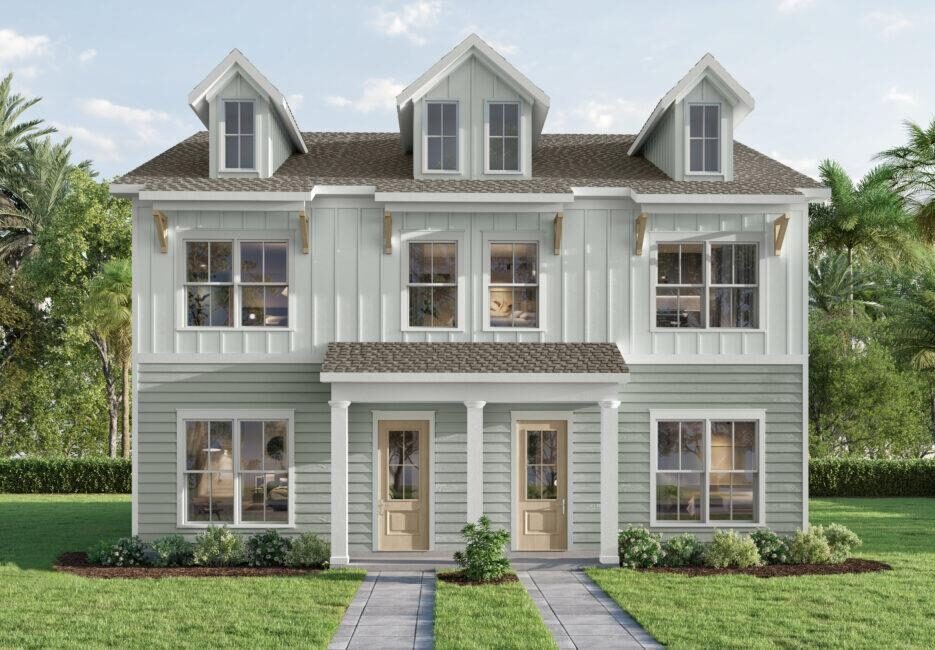 A two-story, light green and white duplex with three dormer windows, two front doors, large windows, and a small front garden with a walkway, surrounded by grass and palm trees.